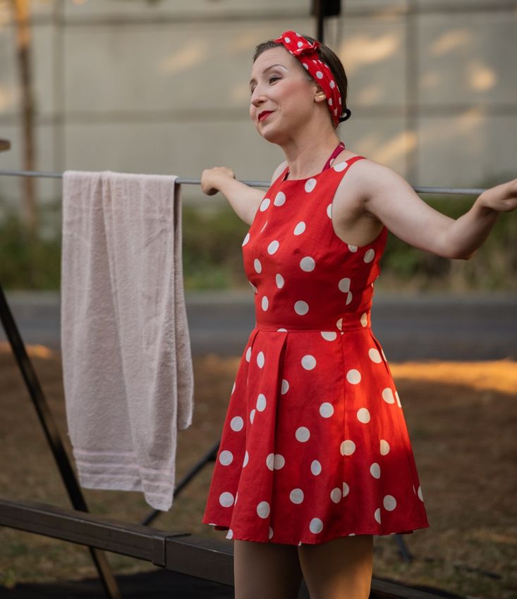 Alexandra en robe rouge à pois, un bras tendu et l’autre main sur le fil derrière elle.