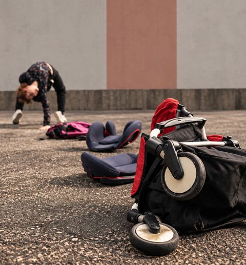 Une poussette et des sièges d’enfant au premier plan, une acrobate à l’arrière-plan.