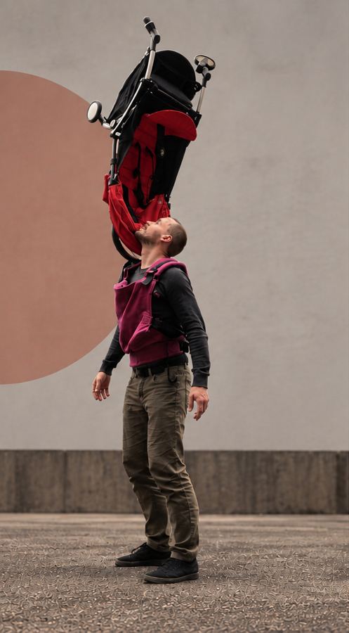Une poussette rouge en équilibre au-dessus du visage du porteur, qui porte un porte-bébé rose.