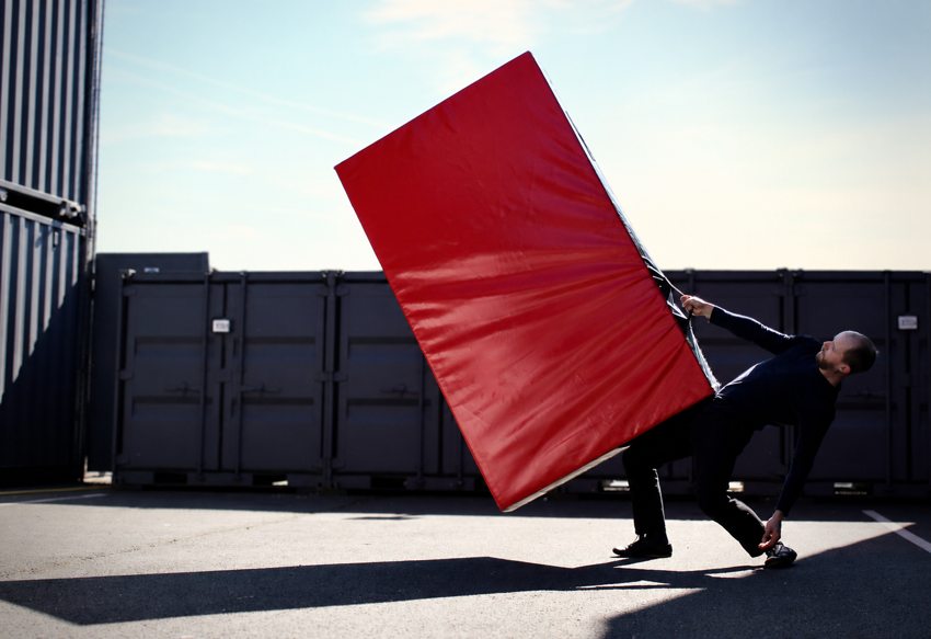 En extérieur, le porteur équilibre le tapis rouge tout en prenant appui sur une main.