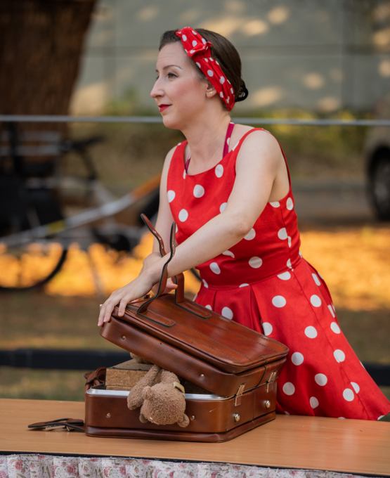 Alex, en robe rouge à pois blancs, ouvre une valise dans Au bout du train.