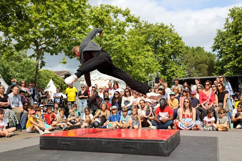 En représentation extérieure, le porteur fait une acrobatie devant les spectateurs réunis autour du tapis.